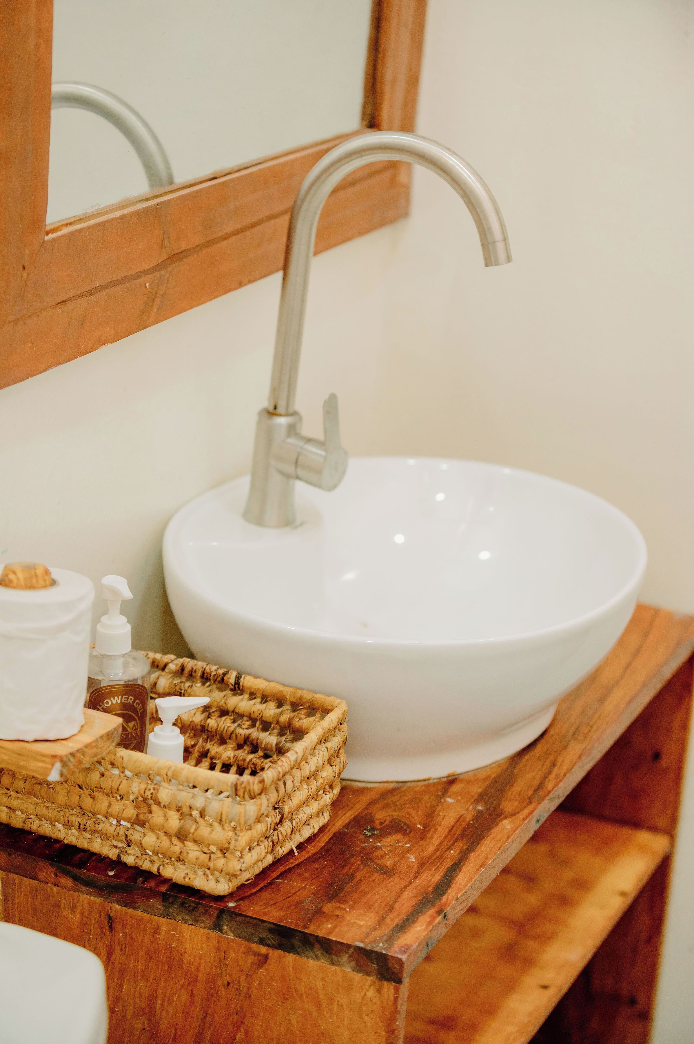 A bathroom with a white sink, a wooden vanity, a mirror, and a wicker basket on the counter.