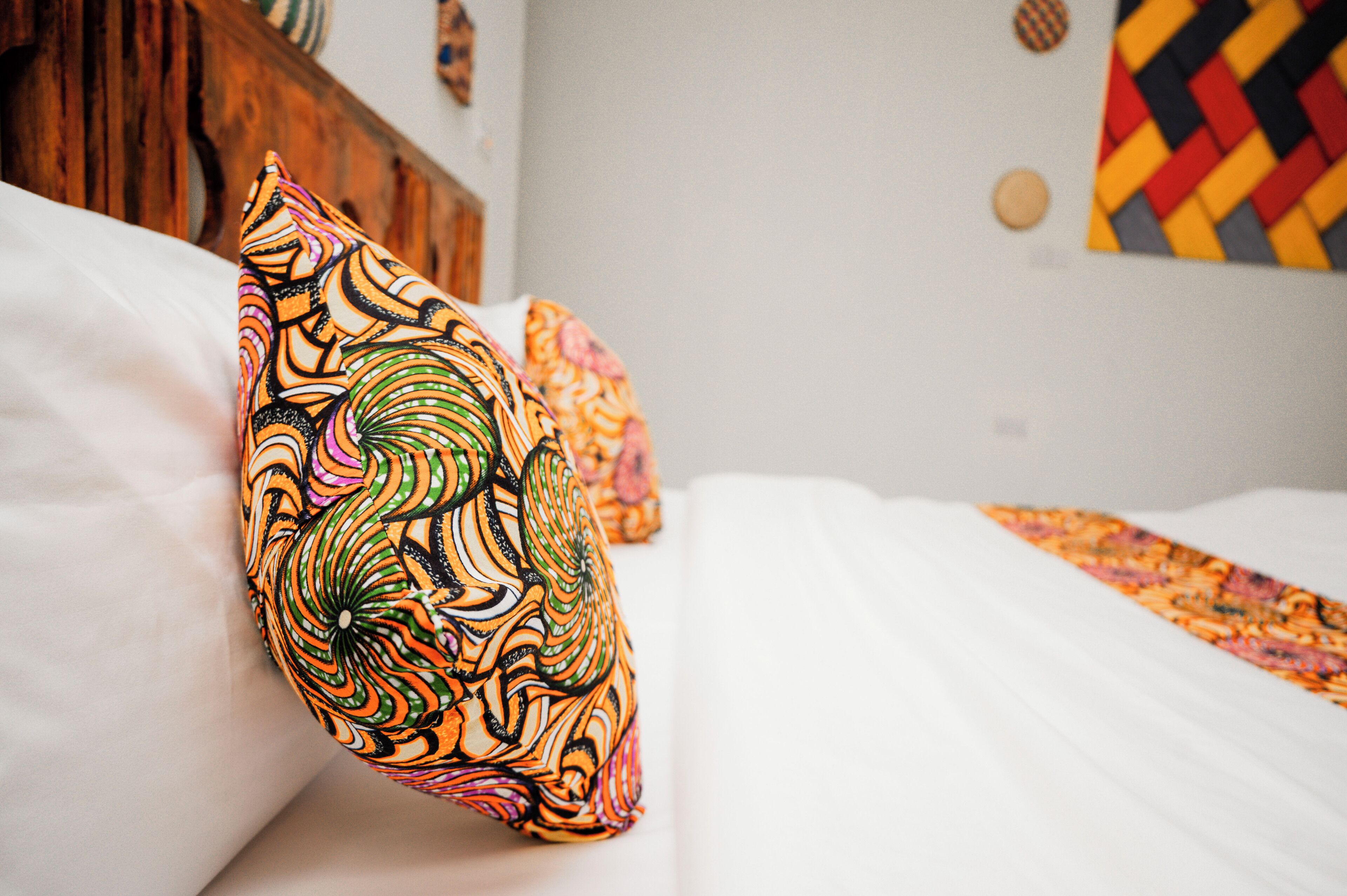 Una cama con sábanas blancas y un cojín estampado y colorido.