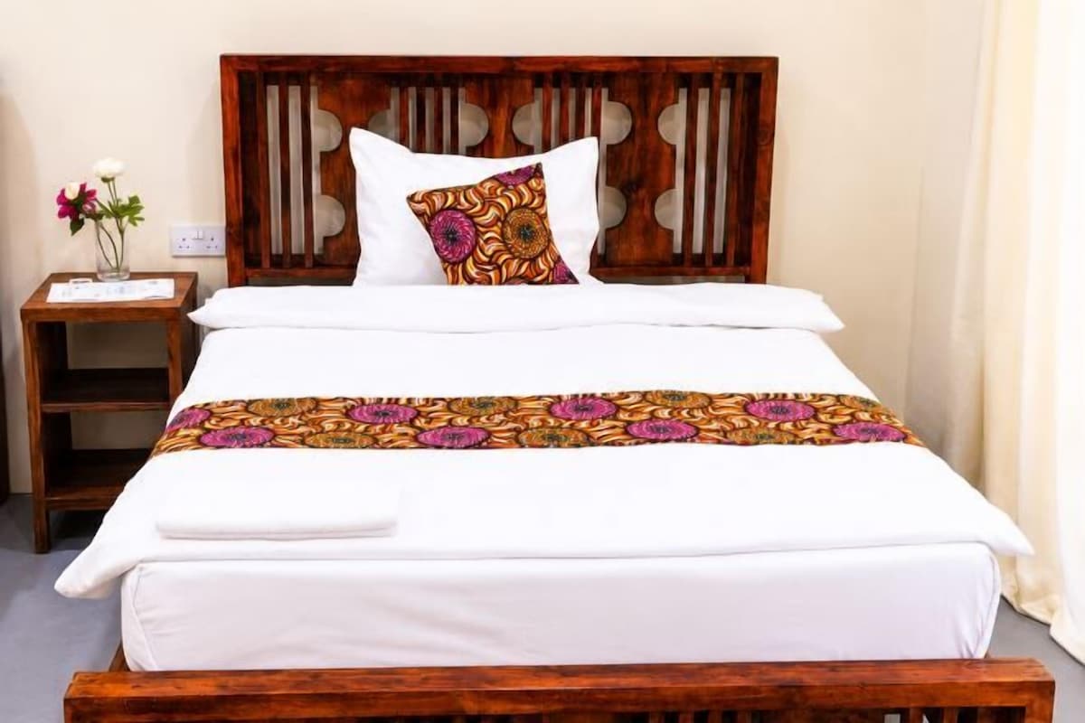 Una cama con cabecera de madera, ropa de cama blanca y una colcha con estampado floral.