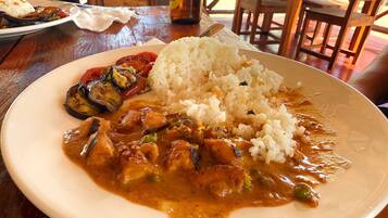 En tallerken mad med ris, grillstegt aubergine og en curryret, serveret på et træbord.