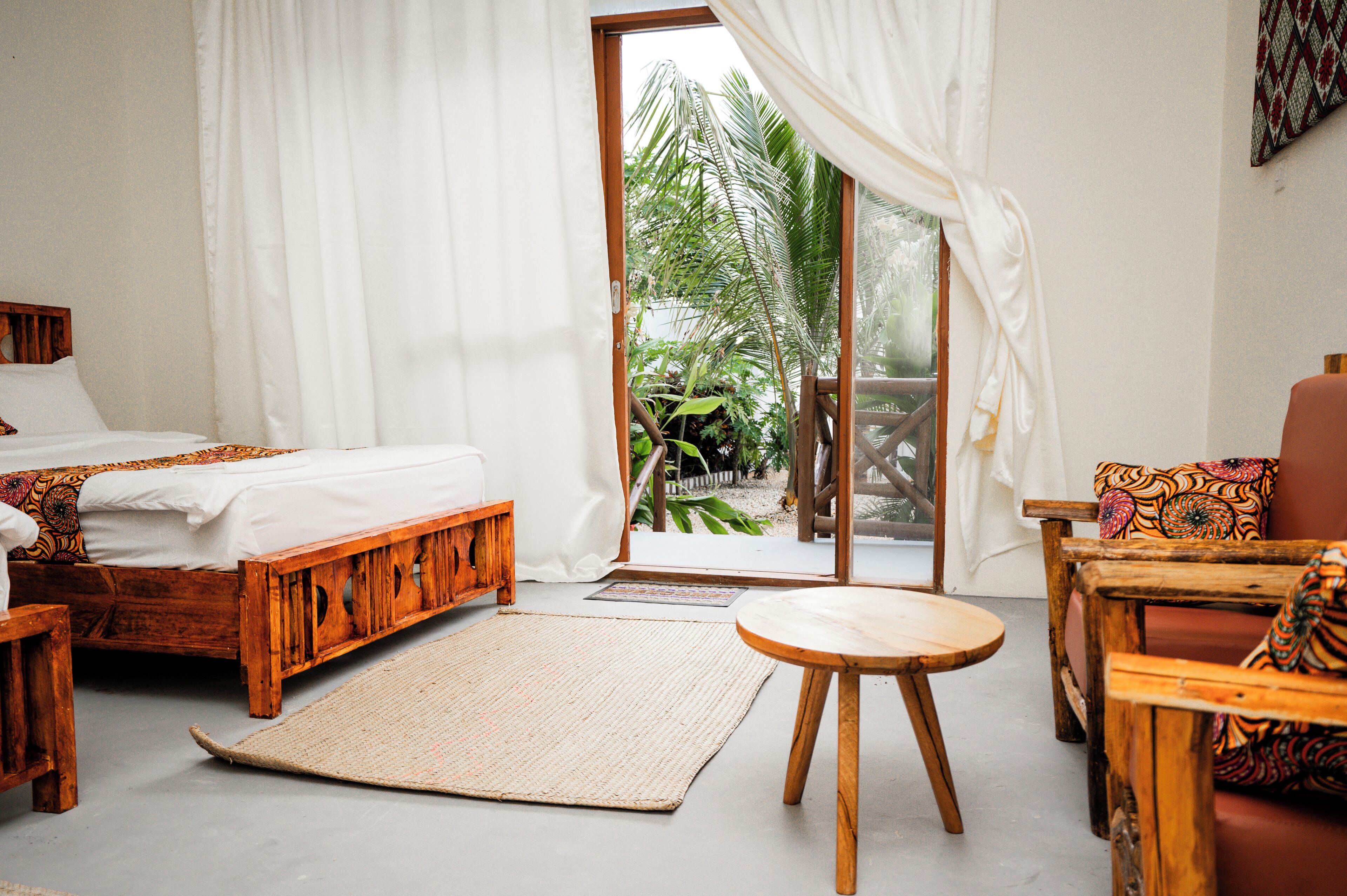A room with a bed, a wooden chair, a small table, and a view of greenery outside.
