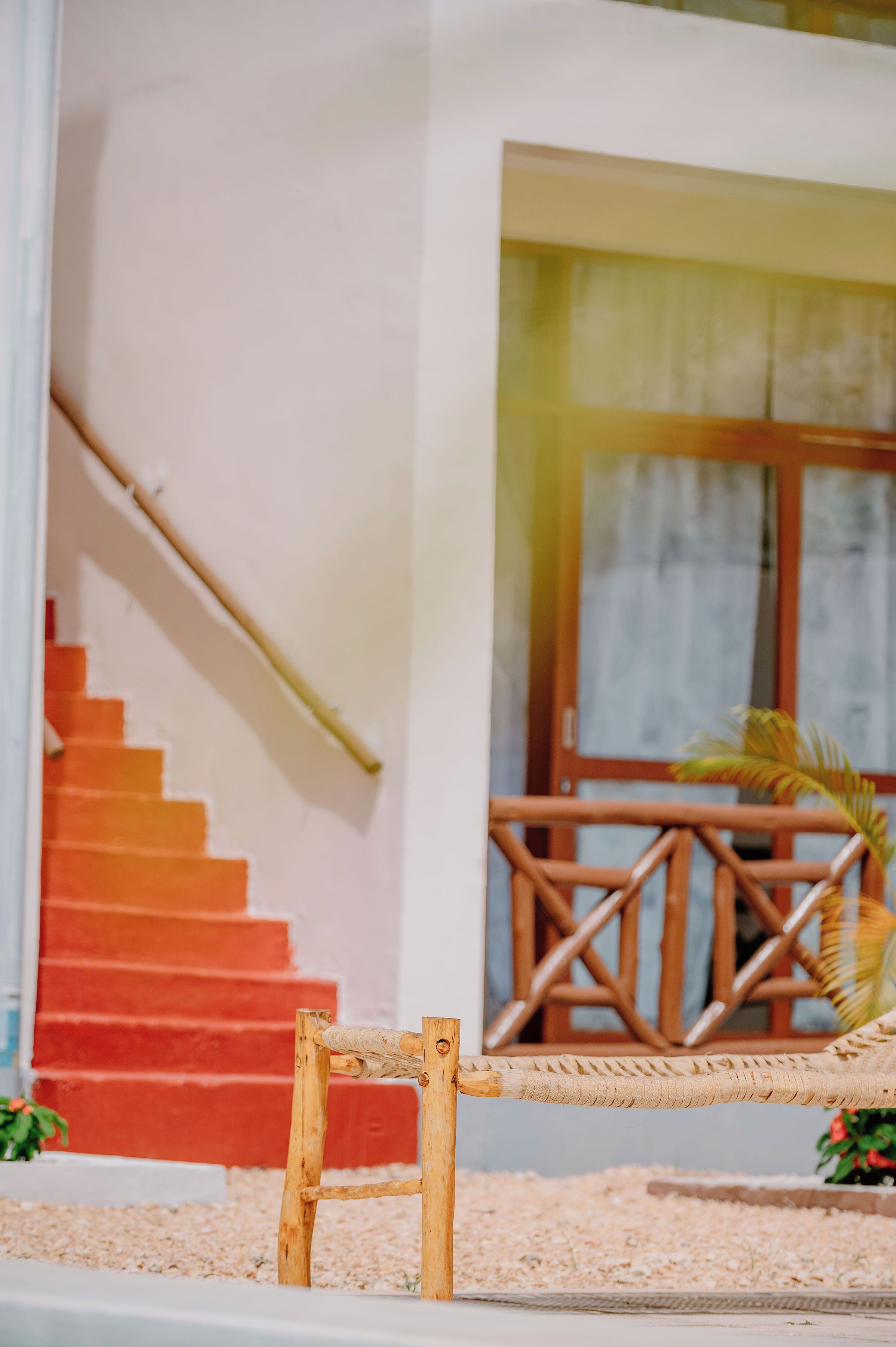 A wooden chair in front of a staircase with red steps, a wooden railing, and a window with a view of a building.