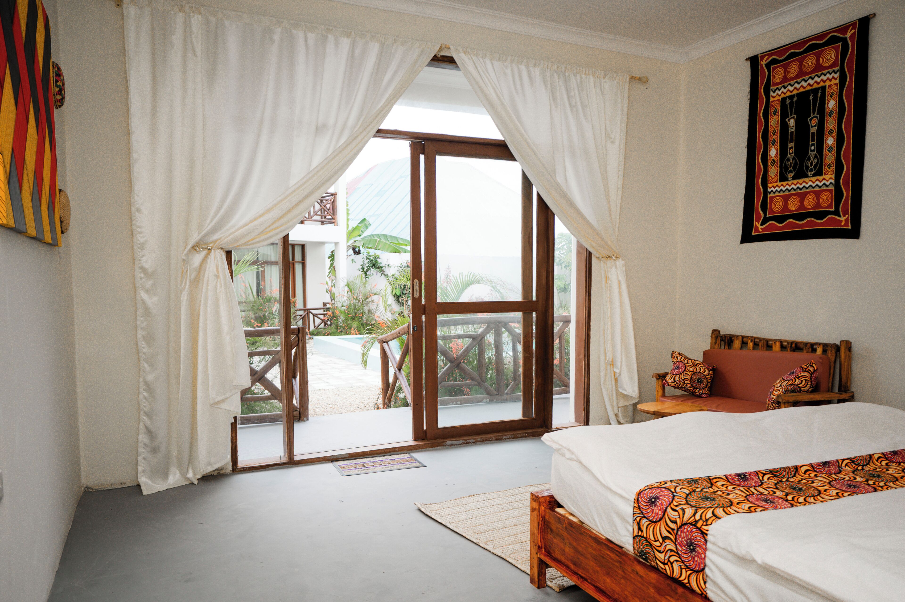 A bedroom with a bed, a wooden headboard, a bench, and a view of a garden through a glass door.