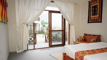 A bedroom with a bed, a wooden headboard, a bench, and a view of a garden through a glass door.