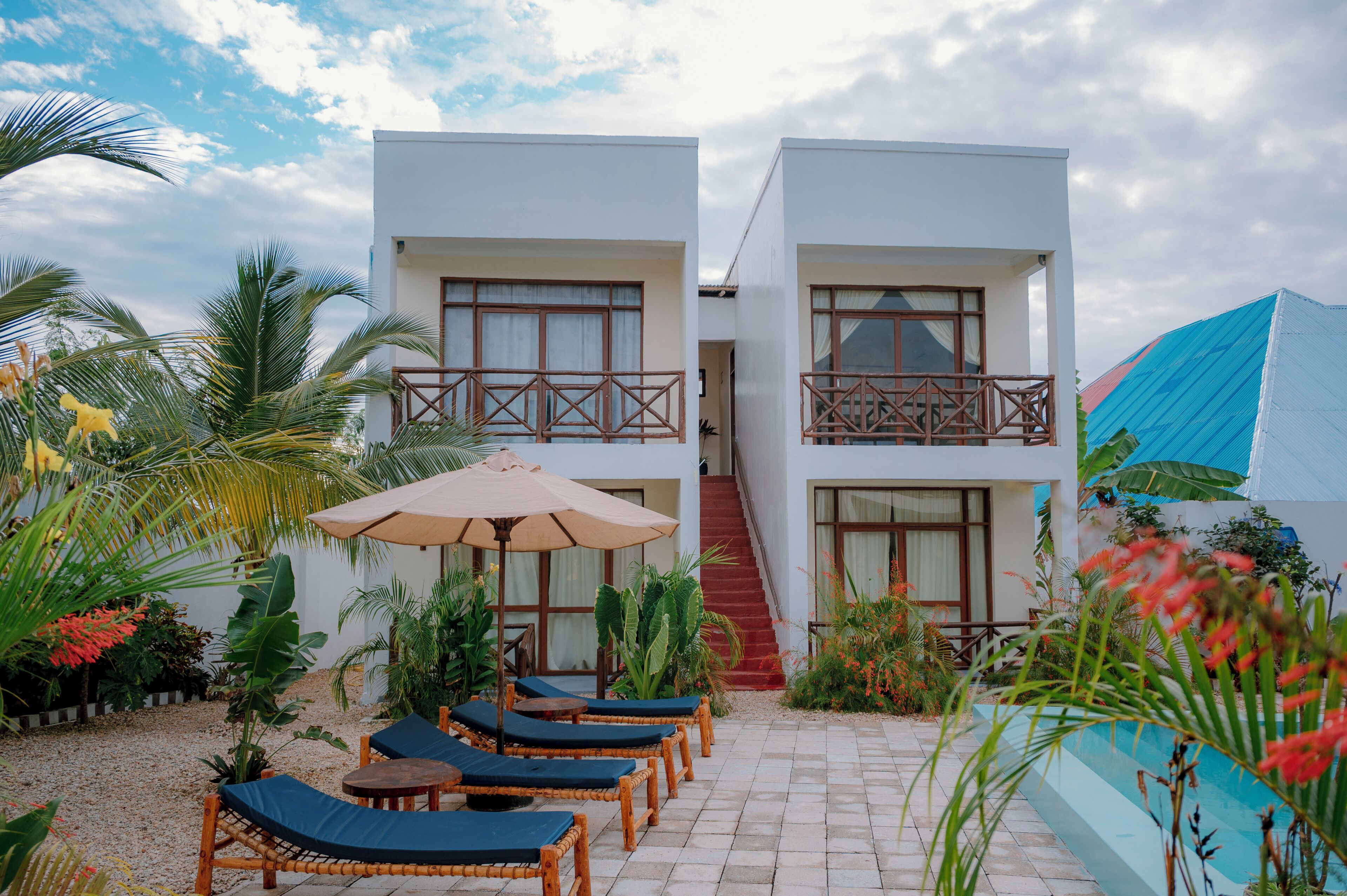 A two-story building with a balcony, a staircase, and a pool area with lounge chairs and an umbrella.