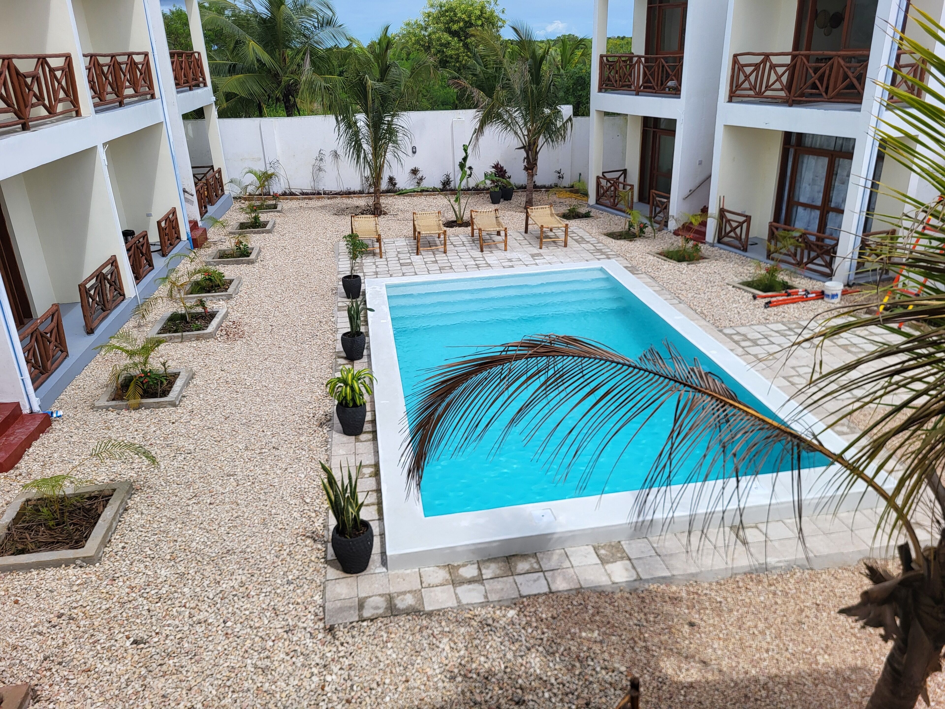 A pool area with a rectangular pool, surrounded by a gravel surface and potted plants.