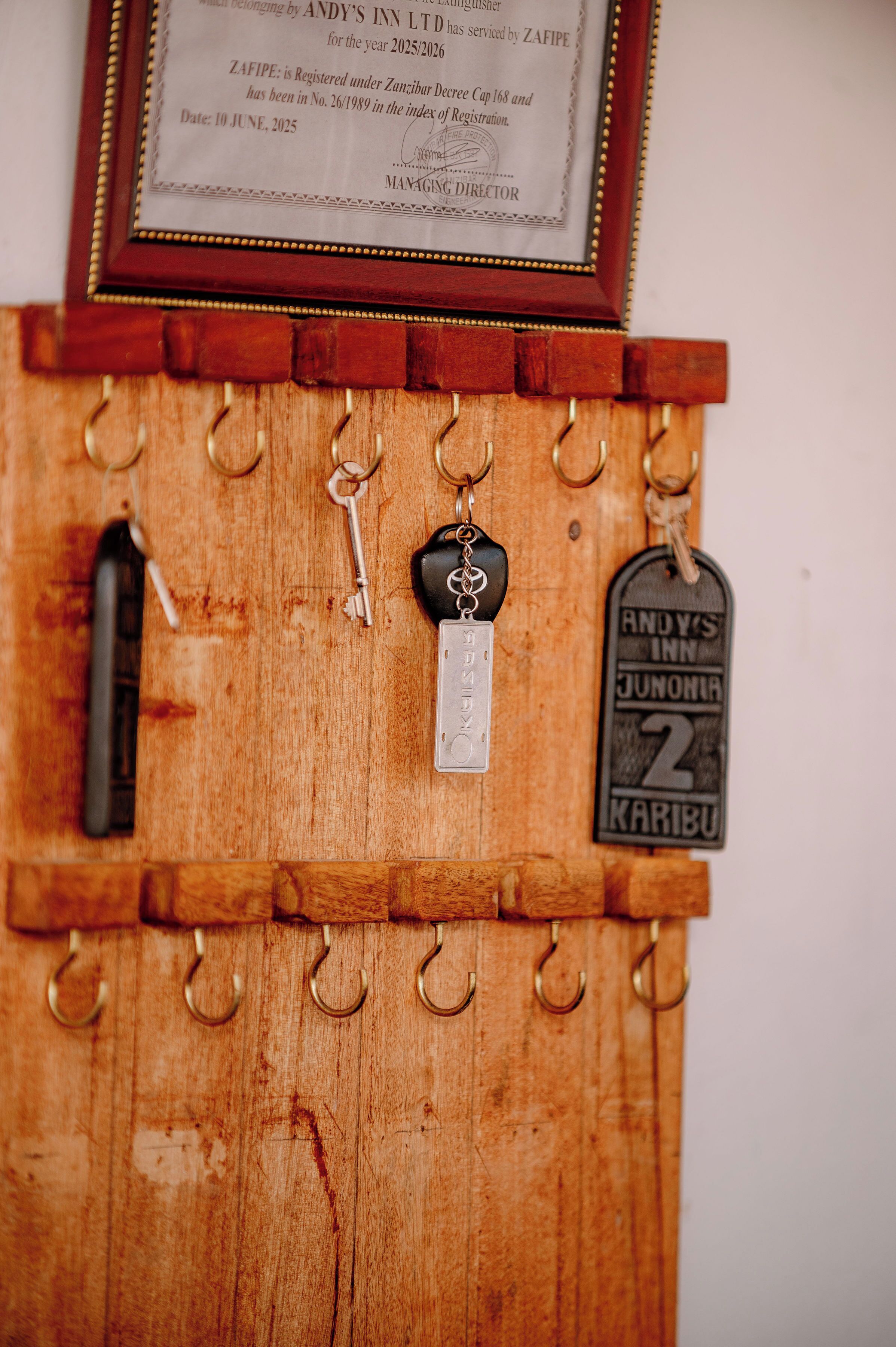 Un perchero de madera con llaves y un llavero, un certificado enmarcado y una etiqueta de llave para el Inn Andy's Junonira 2 Karibu.