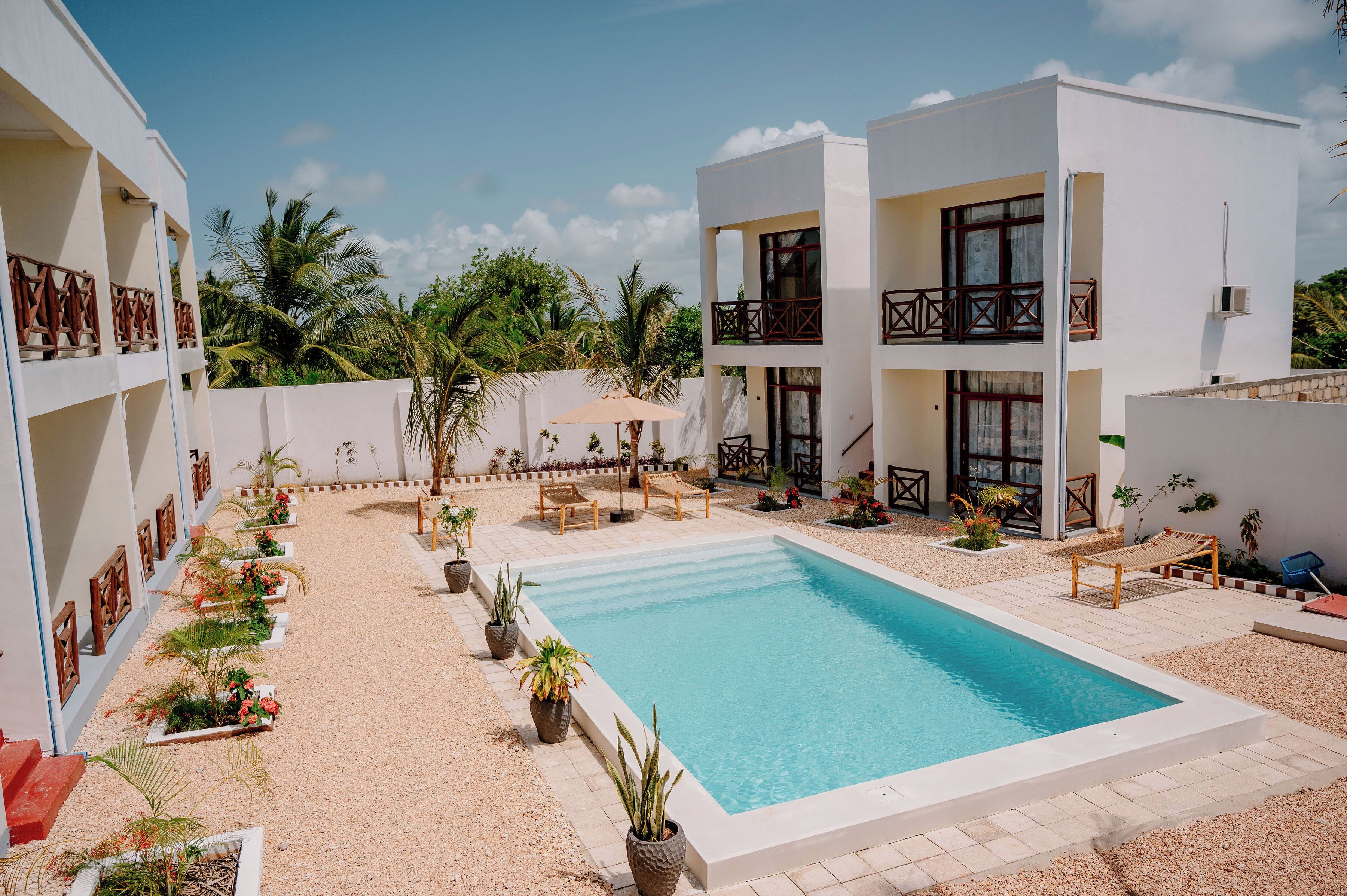 A modern two-story building with a swimming pool, outdoor seating, and potted plants.