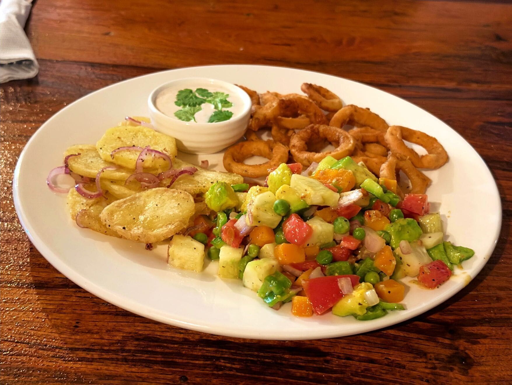 Ein Teller mit Kartoffelspalten, Zwiebelringen und einem Gemischtsalat.