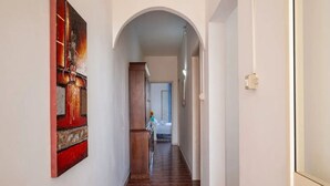 Un pasillo con piso de baldosas, una puerta de madera y una pared blanca con una obra de arte roja y negra.