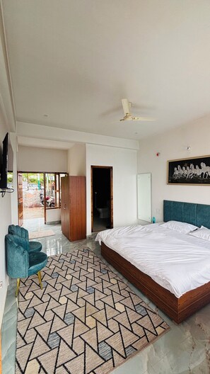 Une chambre avec un grand lit, un ventilateur de plafond, une armoire en bois et une chaise bleue.