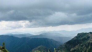 Un paysage montagneux avec une vallée et des montagnes lointaines sous un ciel nuageux.
