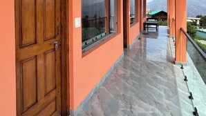 Un couloir avec une porte en bois, de grandes fenêtres et un balcon offrant une vue sur les montagnes.
