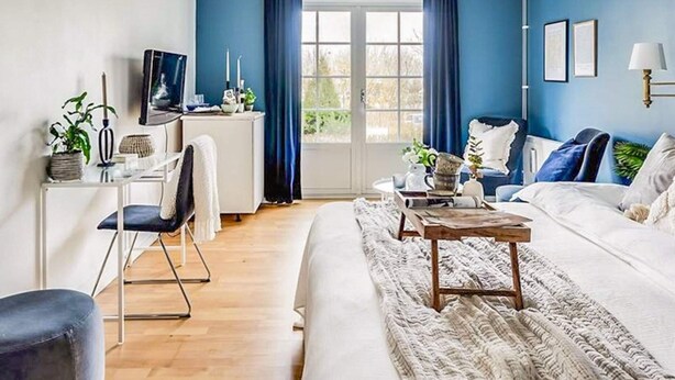 A modern living room with a blue accent wall, a white sofa, a wooden coffee table, and a desk with a chair. - 2 Person Holiday Park Home in Bastad (Bastad)