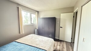 A bedroom with a bed, a wardrobe, a window with curtains, and a door.