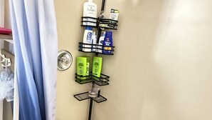 A bathroom with a bathtub, a showerhead, and a shelf with toiletries.