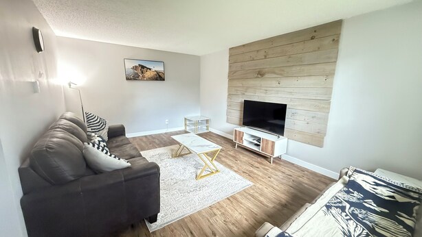A modern living room with a sofa, coffee table, TV stand, and a wooden wall panel.