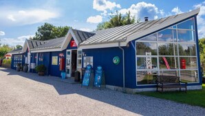 A blue building with a sloped roof and large windows, likely a restaurant or cafe, with outdoor seating and a gravel path in front. - 6 Person Holiday Park Home in Vipperod (Vipperod)