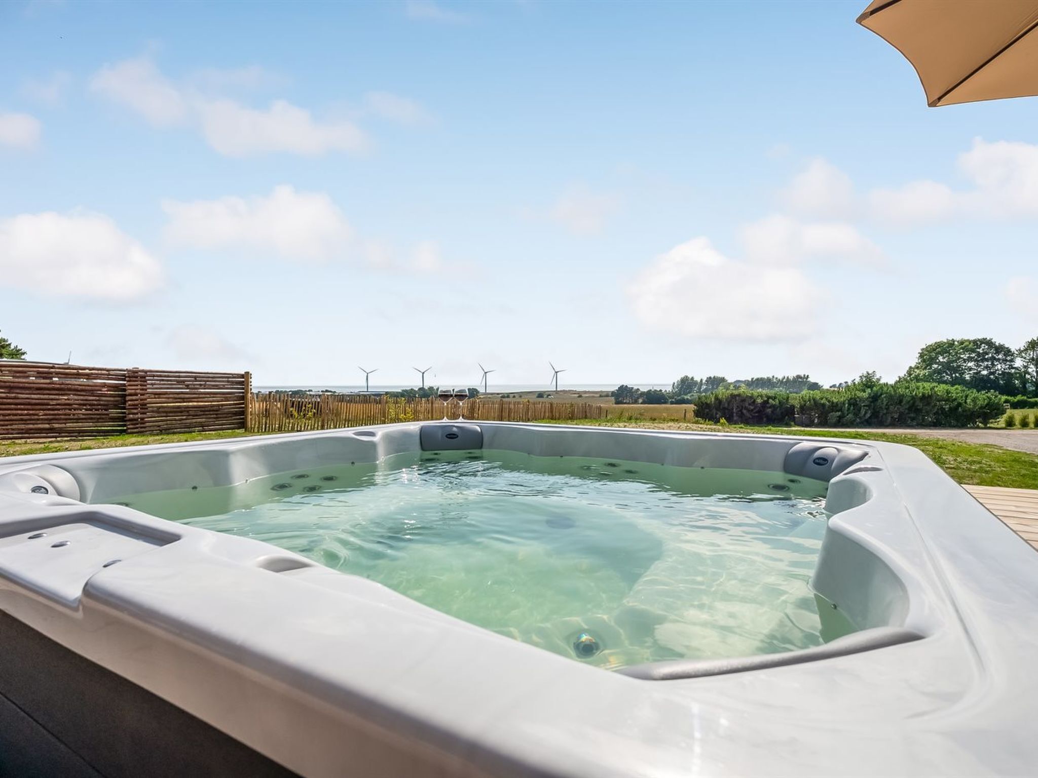 Un bain à remous avec une terrasse en bois et une vue sur les éoliennes au loin.