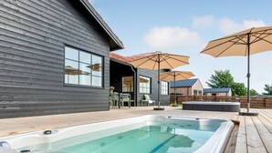 A modern outdoor hot tub area with a wooden deck, a covered seating area, and a view of a house in the background. - "Adia" - 650m from the sea by Interhome (Ebeltoft)
