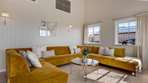 A spacious living room with a mustard-colored sectional sofa, a round glass coffee table, and a large window providing natural light. - "Adia" - 650m from the sea by Interhome (Ebeltoft)