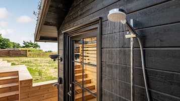 Une cabane en bois avec une porte en verre, une douche et une terrasse en bois.