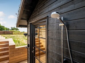 Eine Holzhütte mit Glastür, Duschkopf und einer Holzdar Terrasse.