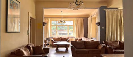 A spacious living room with multiple seating areas, a central coffee table, and a large window providing natural light.