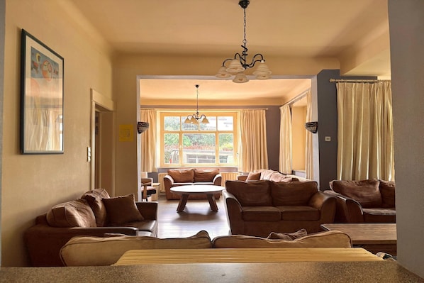 A spacious living room with multiple seating areas, a central coffee table, and a large window providing natural light.