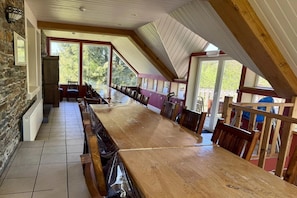 A long wooden table with chairs in a room with stone walls and large windows. - Group Home in La Roche with sauna (La Roche-en-Ardenne)
