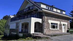 Un bâtiment en pierre de deux étages, doté d’un balcon à l’étage supérieur, d’un porche à l’avant et d’un petit garage attenant.