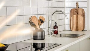 A kitchen with white tiles, a stainless steel sink, a wooden cutting board, and a spice rack with wooden utensils. - 2 Person Holiday Park Home in Bastad (Bastad)