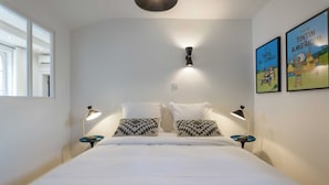 A hotel room with a large bed, two bedside tables with lamps, a wall-mounted light, and two framed posters. - DIFY Vitton - Masséna (Lyon)