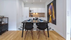 A modern kitchen with white cabinets, a black and white checkered floor, and a dining area with a black table and chairs. - DIFY Vitton - Masséna (Lyon)