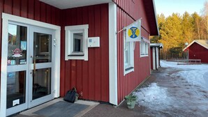 A red building with a white door and windows, a green bucket, and a sign with a blue and yellow emblem. - 2 Person Holiday Park Home in Orsa (Orsa)