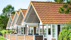 En rad med trähus med sadeltak och stora fönster, placerade på en gräsyta omgiven av träd.