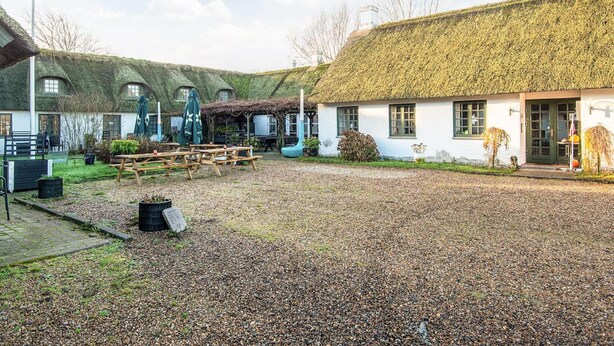Een erf met gebouwen met rieten daken, picknicktafels en terrasstoelen.