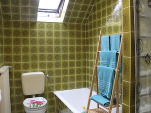 Ein Badezimmer mit grün gemusterten Fliesen, einer weißen Toilette und einem Holzstuhl mit blauem Handtuch.