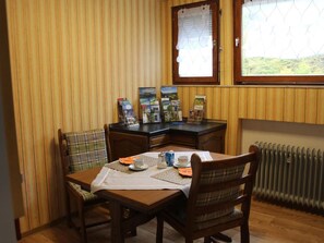 Ein Essbereich mit einem Holztisch, karierten Stühlen und einem Fenster mit Blick auf Grünflächen.