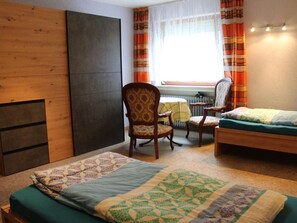 Ein Schlafzimmer mit einem Bett, zwei Stühlen, einem Heizkörper und einem Fenster mit Vorhängen.