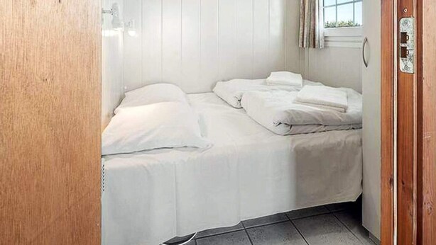 Ein kleines Zimmer mit einem Einzelbett, weißer Bettwäsche, einer Holztür und einem Fenster mit Vorhängen.