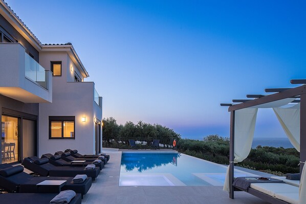 A modern outdoor pool area with lounge chairs and a canopy bed, overlooking a scenic view.