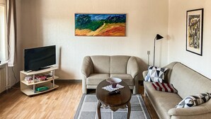 A living room with a beige sofa, a coffee table, a television on a stand, and a painting on the wall. - 2 bedroom stunning home in Harboøre (Harboøre)