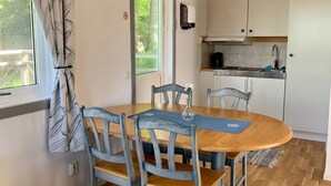 A dining area with a wooden table and chairs, a vase with flowers, and a view of the kitchen in the background. - 2 Person Holiday Park Home in Stenungsund (Stenungsund)
