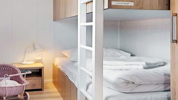 Habitación con literas, cabecera de madera, mesita de noche con lámpara y una silla de mimbre.