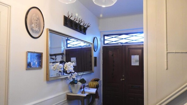A hallway with a large mirror, a framed photo, a small table with a vase of flowers, and a door with a sign. - 2 Person Holiday Park Home in Tranekaer (Tranekaer)