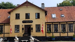 A building with a yellow facade, a red-tiled roof, and two flags. - 2 Person Holiday Park Home in Tranekaer (Tranekaer)