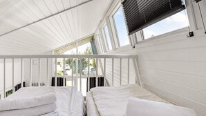 A room with two beds, white bedding, and a view of the outside through a window with blinds.