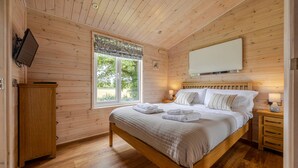Ein Schlafzimmer mit Holzwandverkleidung, einem Bett, Nachttischen, einem Fernseher und einem Fenster.