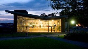 Un bâtiment moderne doté de grandes fenêtres en verre, d’un toit plat et d’une entrée bien éclairée.
